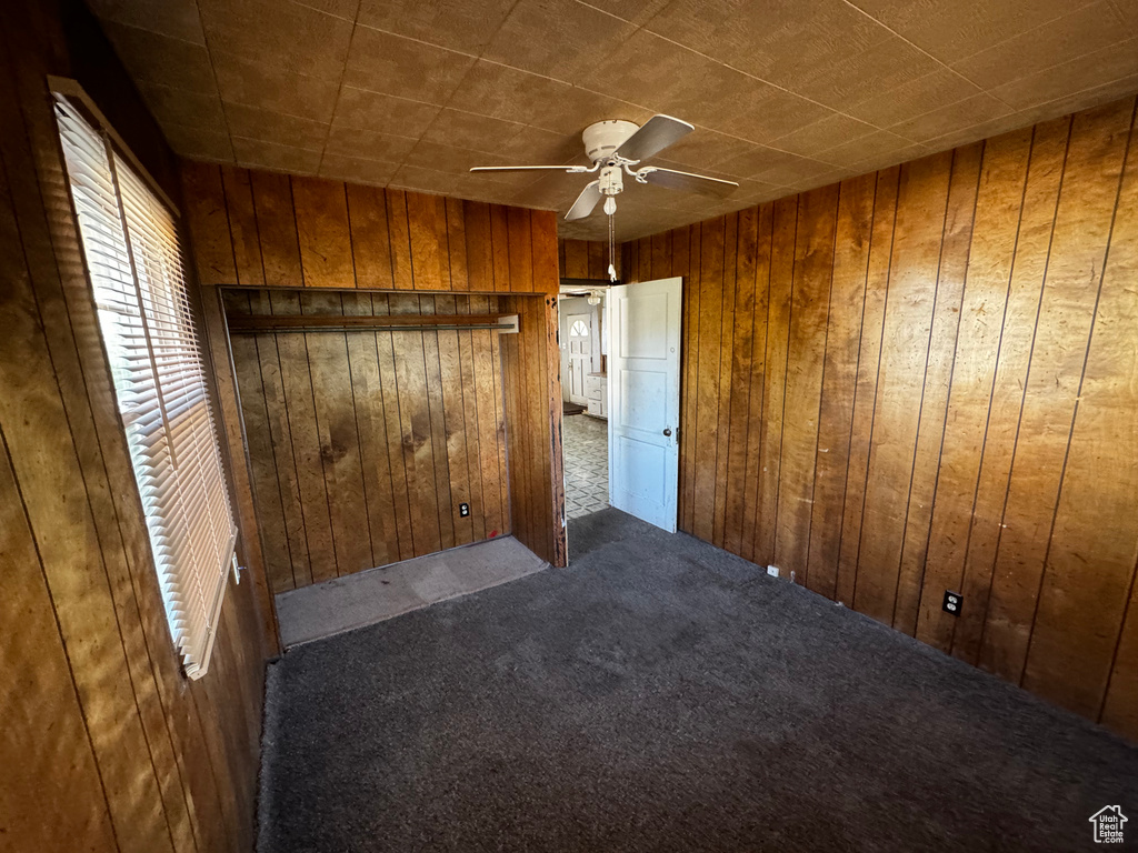 Unfurnished bedroom with wooden walls, ceiling fan, and dark carpet