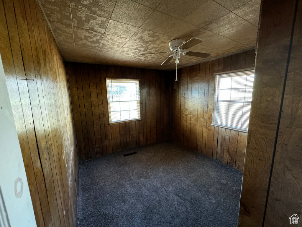 Carpeted spare room featuring wooden walls and ceiling fan