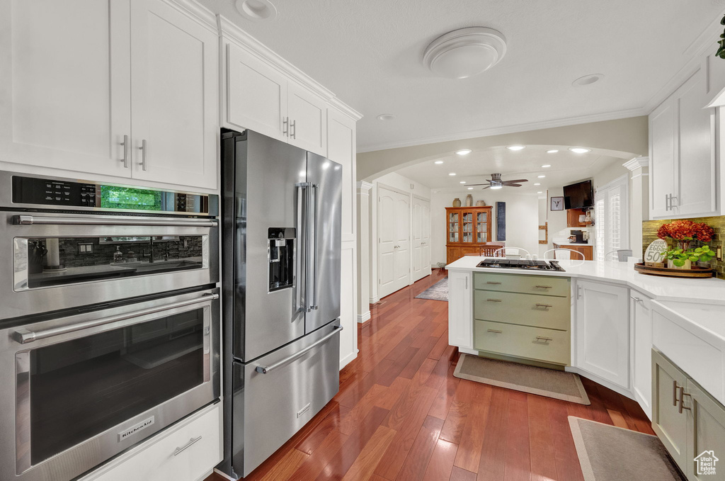 Kitchen with kitchen peninsula, stainless steel appliances, ceiling fan, hardwood / wood-style floors, and white cabinetry