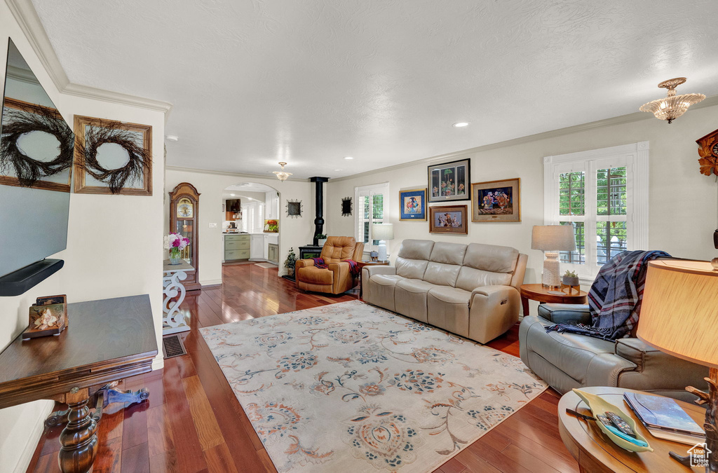 Living room featuring a notable chandelier, dark wood-type flooring, a wood stove, and crown molding