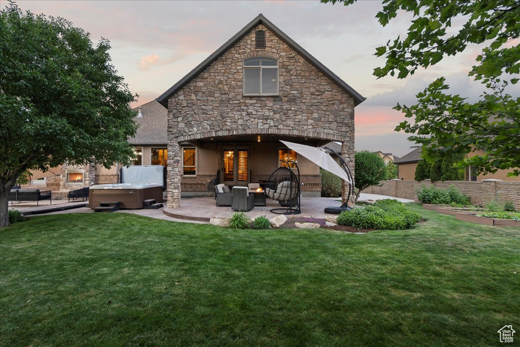 Back house at dusk with a yard, an outdoor hangout area, a patio area, and a hot tub