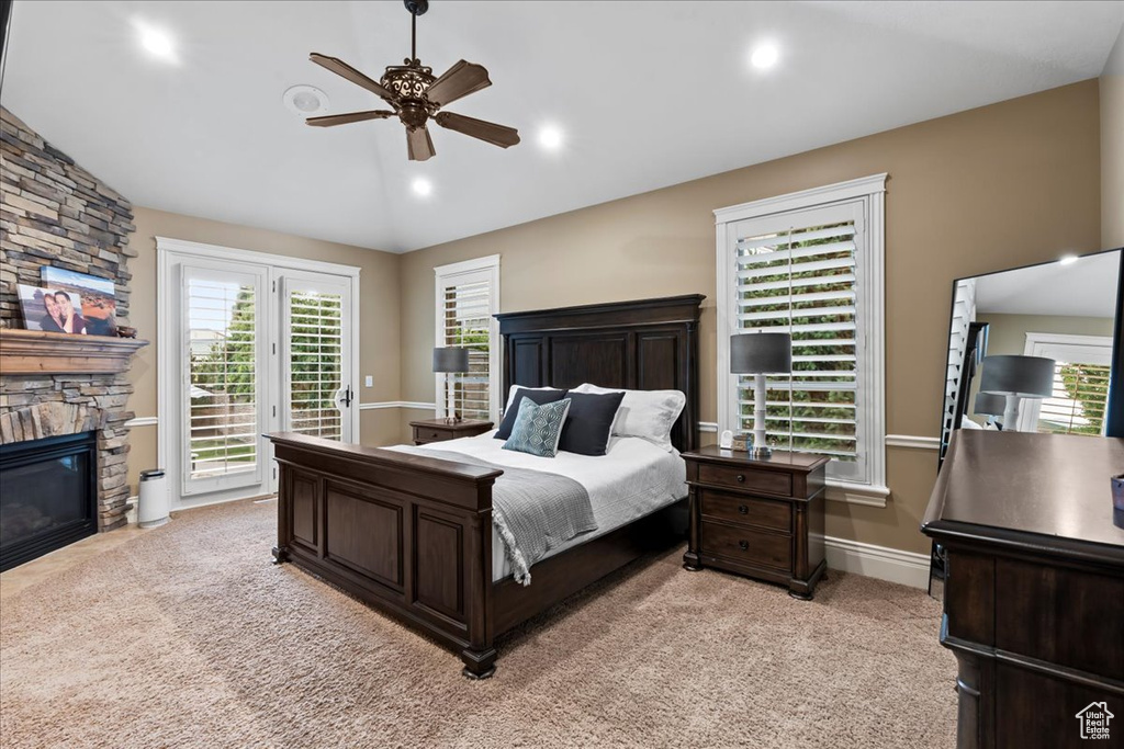 Carpeted bedroom featuring a stone fireplace, ceiling fan, lofted ceiling, and access to exterior