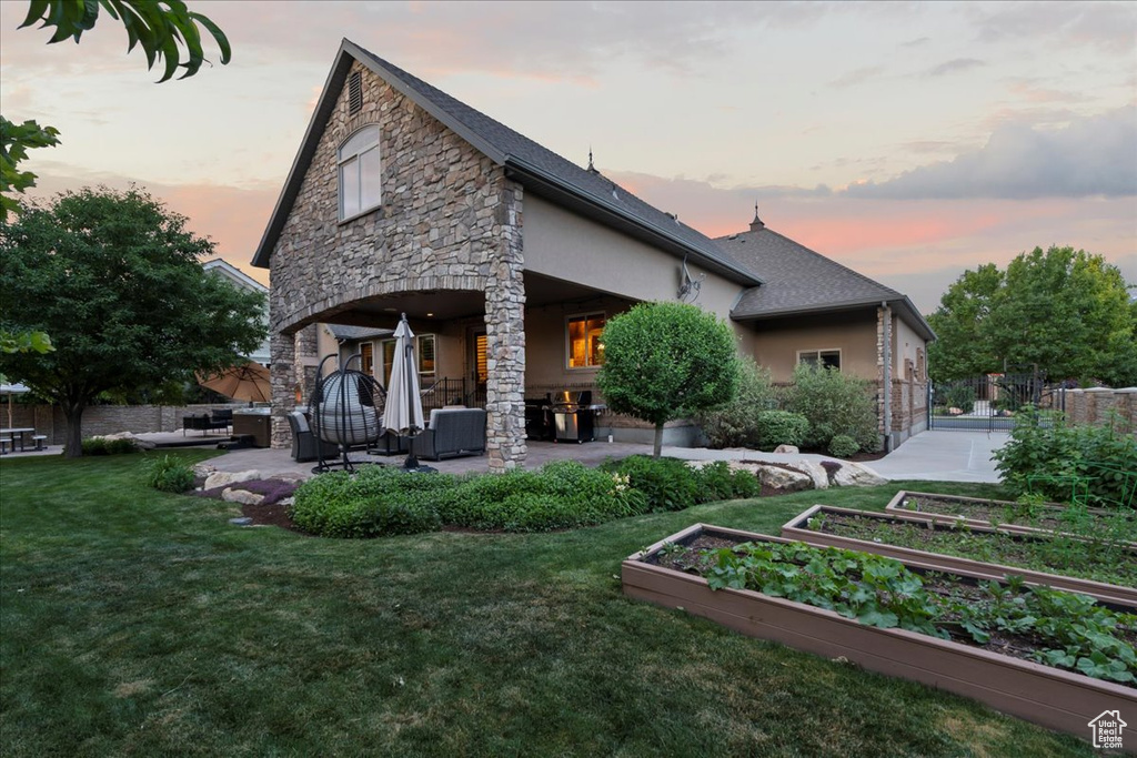 Back house at dusk featuring a lawn and a patio area