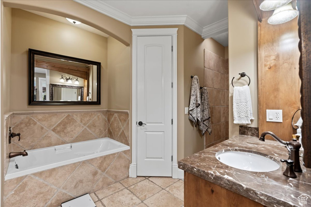 Bathroom with a relaxing tiled bath, tile flooring, vanity with extensive cabinet space, and crown molding