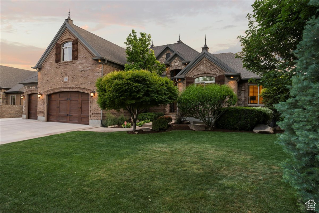 French country style house featuring a garage and a lawn