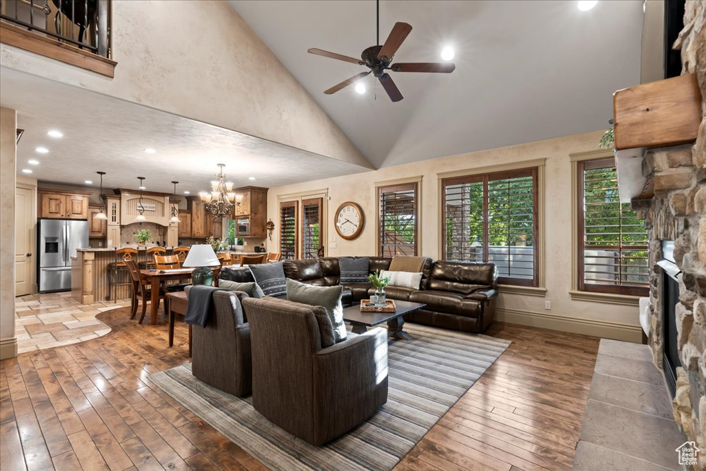 Living room featuring high vaulted ceiling, a fireplace, light wood-type flooring, and ceiling fan with notable chandelier