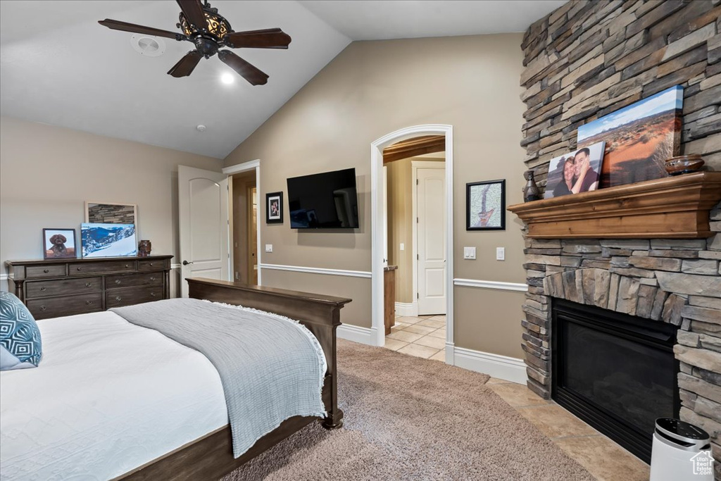 Tiled bedroom featuring a stone fireplace, ceiling fan, and lofted ceiling