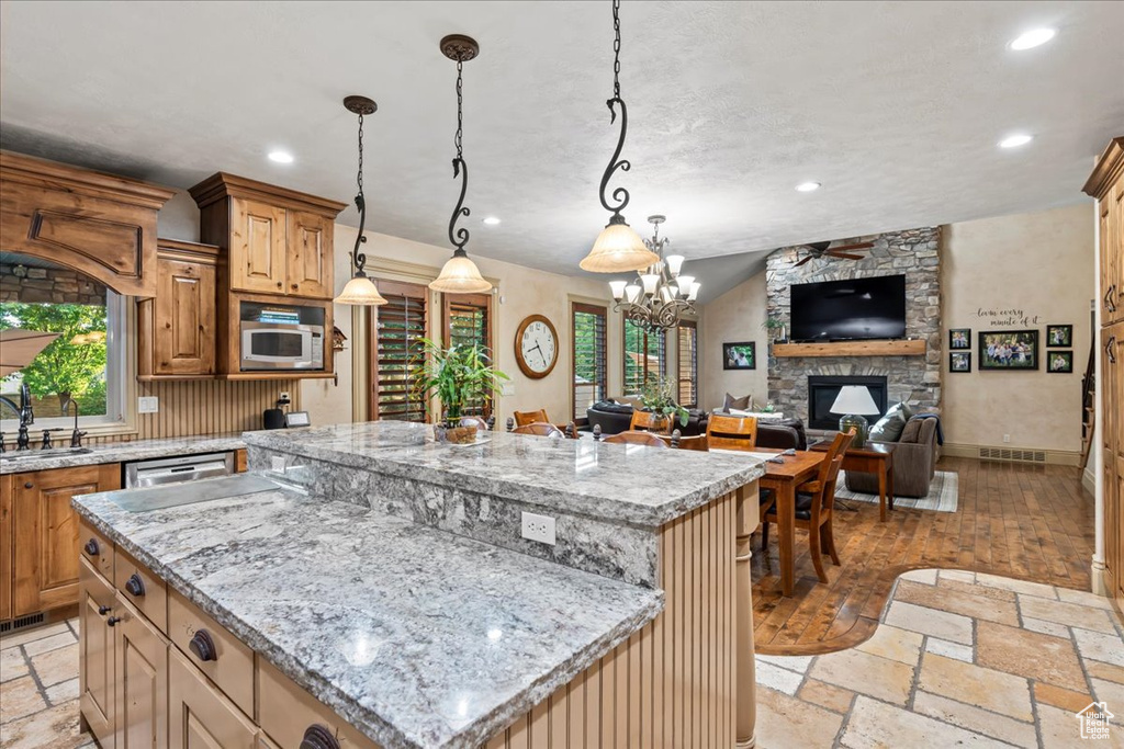 Kitchen featuring a center island, a fireplace, stainless steel appliances, decorative light fixtures, and light tile floors