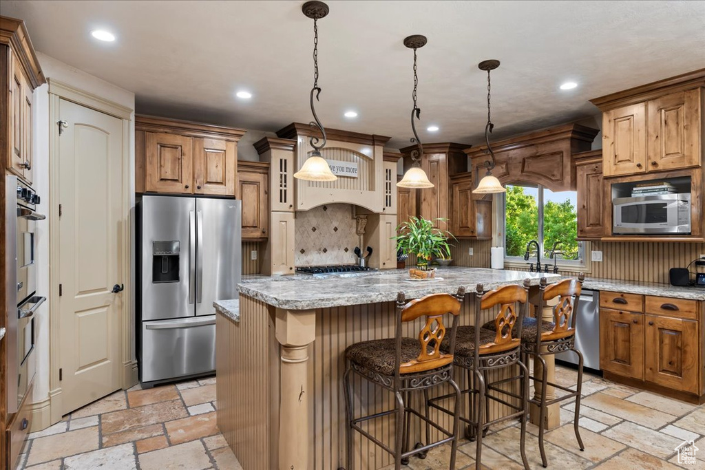 Kitchen featuring light stone countertops, stainless steel appliances, light tile flooring, a kitchen island, and backsplash