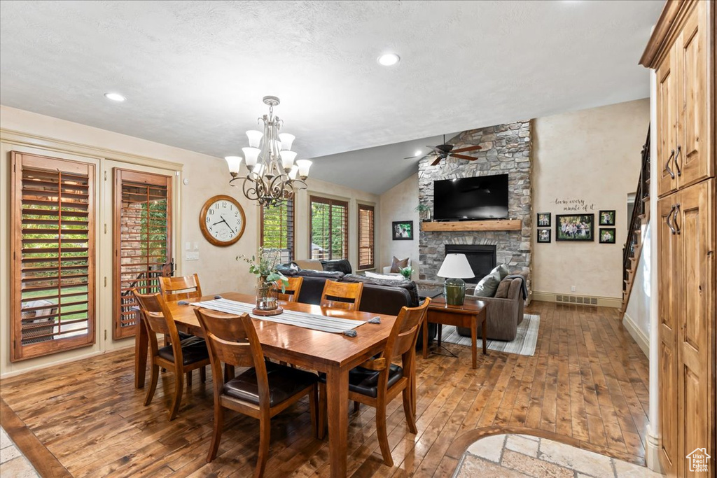 Dining space featuring a stone fireplace, hardwood / wood-style flooring, lofted ceiling, and ceiling fan with notable chandelier