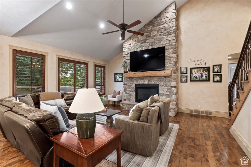 Living room featuring a stone fireplace, high vaulted ceiling, dark hardwood / wood-style floors, and ceiling fan