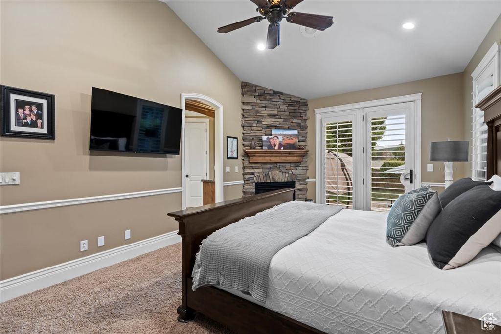 Carpeted bedroom featuring a stone fireplace, ceiling fan, and vaulted ceiling