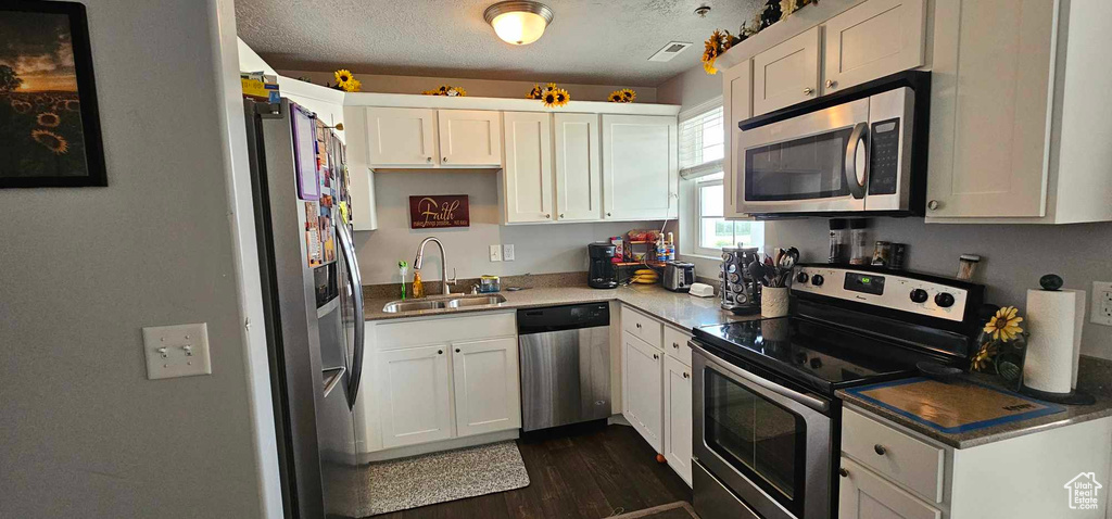 Kitchen featuring white cabinetry, a textured ceiling, dark wood-type flooring, appliances with stainless steel finishes, and sink