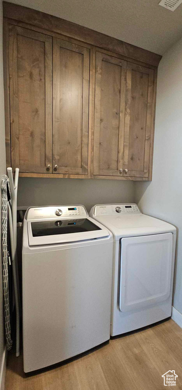 Clothes washing area featuring washing machine and dryer, light hardwood / wood-style floors, and cabinets