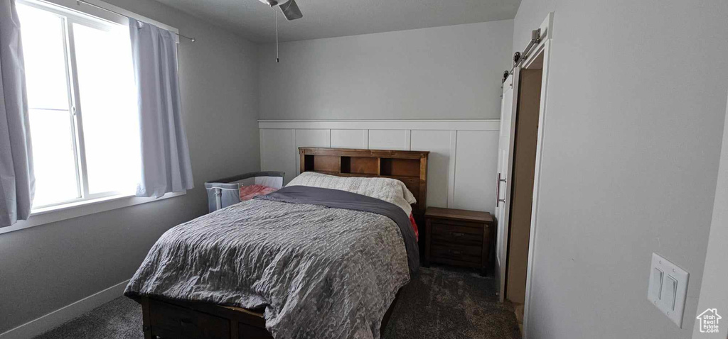 Bedroom with dark carpet, a barn door, and ceiling fan