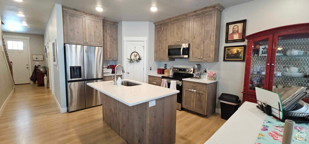 Kitchen with an island with sink, stainless steel appliances, light hardwood / wood-style floors, and sink