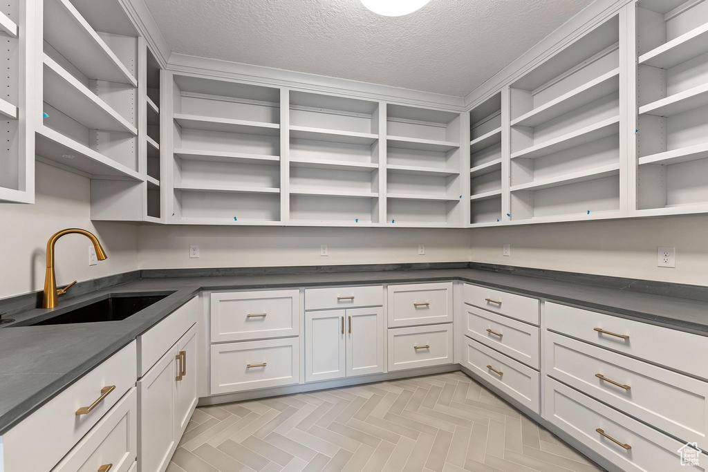 Interior space featuring a textured ceiling, white cabinets, sink, and light parquet floors