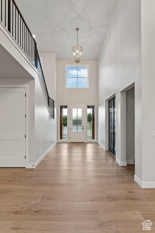 Foyer with a towering ceiling, an inviting chandelier, and light wood-type flooring