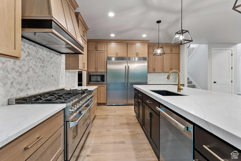 Kitchen with sink, light wood-type flooring, custom exhaust hood, tasteful backsplash, and built in appliances