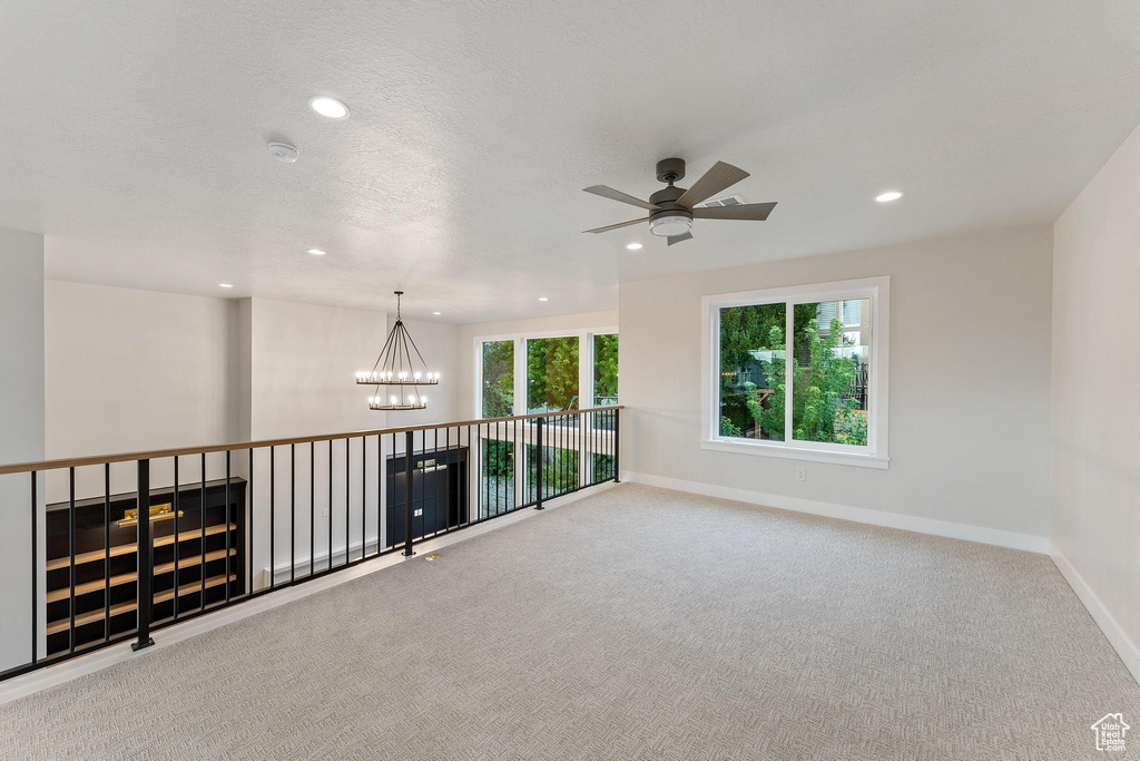 Carpeted empty room with ceiling fan with notable chandelier