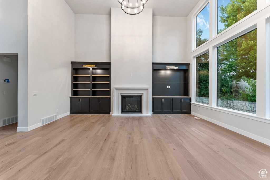 Unfurnished living room with a high ceiling, light hardwood / wood-style floors, a healthy amount of sunlight, and a chandelier