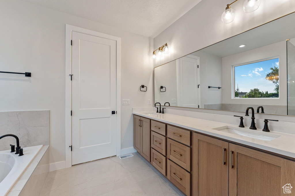 Bathroom featuring a relaxing tiled tub, double vanity, and tile patterned floors