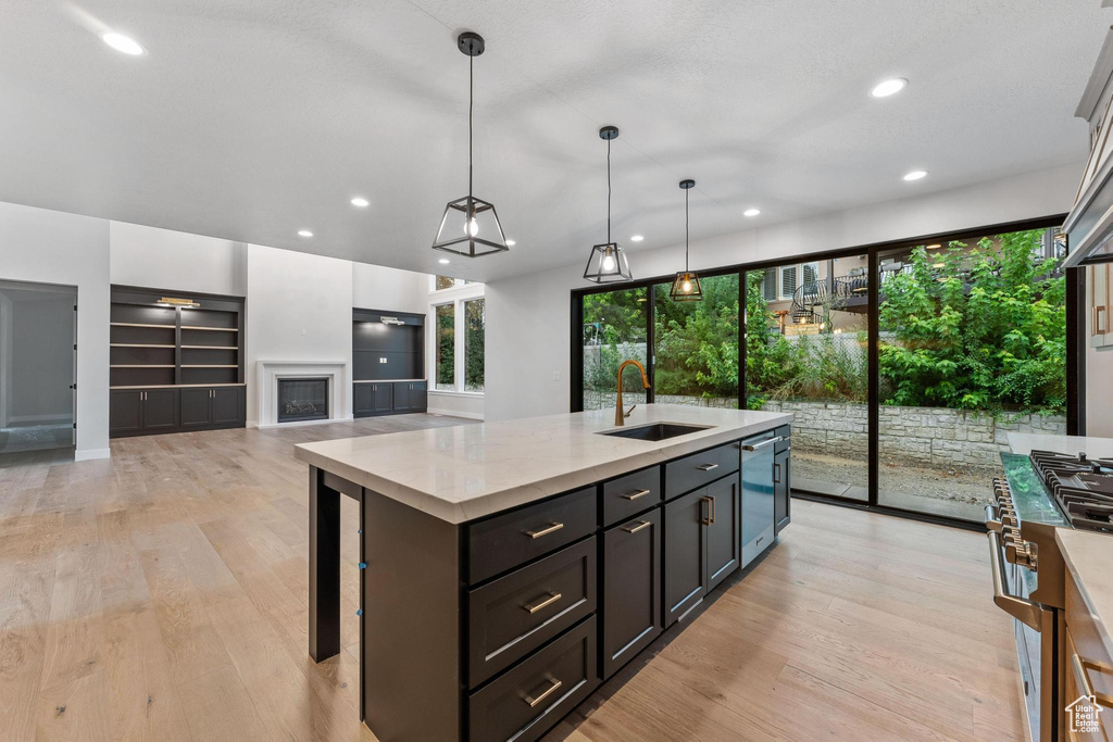 Kitchen with sink, built in shelves, light wood-type flooring, an island with sink, and pendant lighting