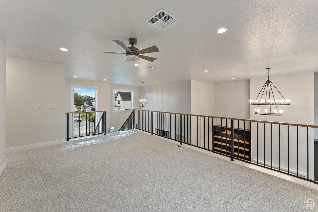 Hallway featuring carpet flooring, a textured ceiling, and a notable chandelier