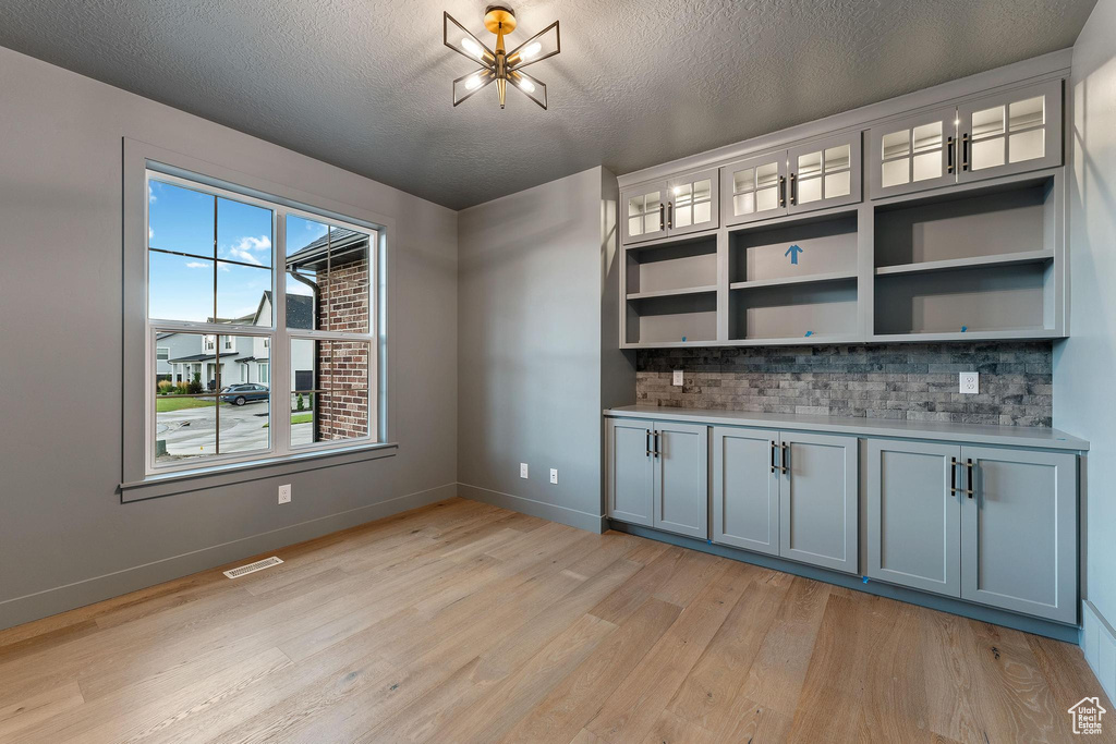 Bar featuring backsplash, a healthy amount of sunlight, a chandelier, and light wood-type flooring