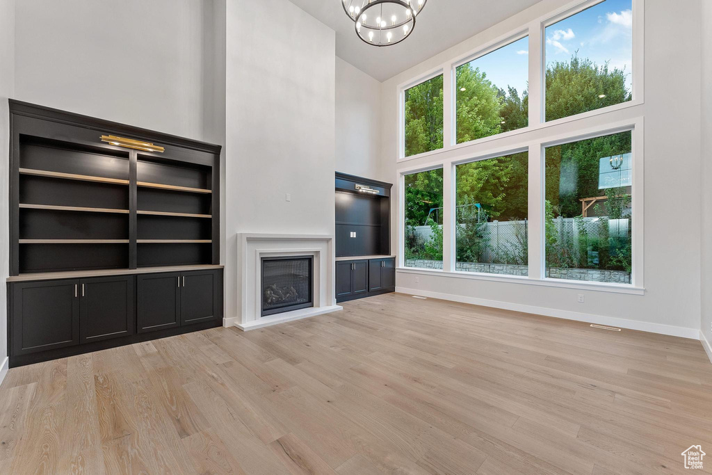 Unfurnished living room featuring a towering ceiling, light wood-type flooring, and a healthy amount of sunlight