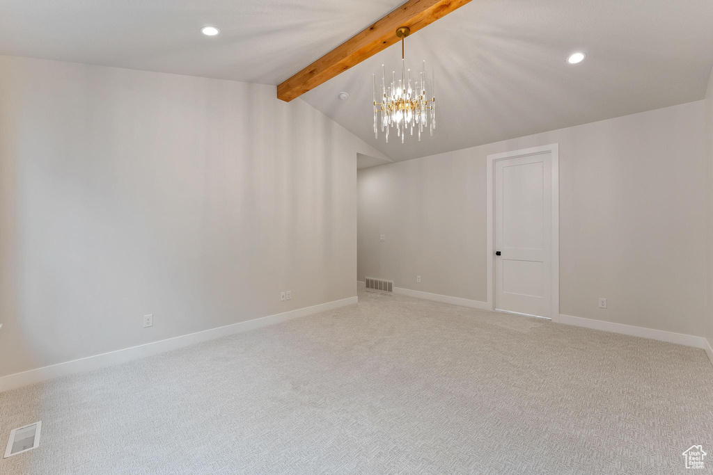 Empty room featuring carpet flooring, vaulted ceiling with beams, and a notable chandelier