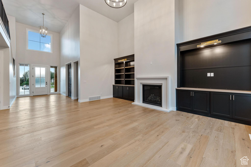 Unfurnished living room featuring light hardwood / wood-style floors, a high ceiling, and a notable chandelier