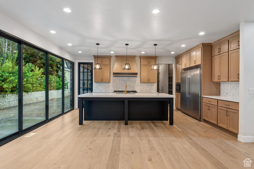 Kitchen with appliances with stainless steel finishes, premium range hood, light hardwood / wood-style floors, and tasteful backsplash