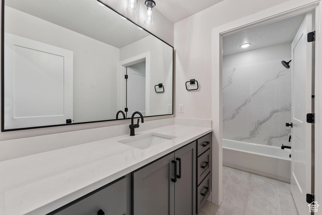 Bathroom with tile patterned flooring, tiled shower / bath, a textured ceiling, and vanity