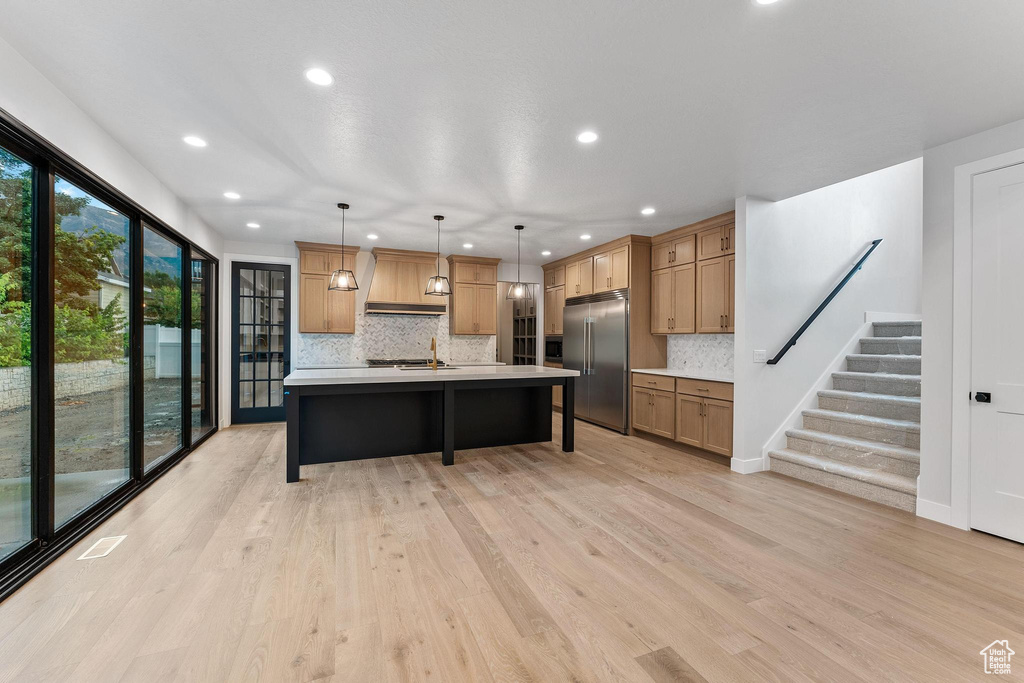 Kitchen featuring decorative backsplash, light hardwood / wood-style floors, stainless steel built in fridge, decorative light fixtures, and a center island with sink