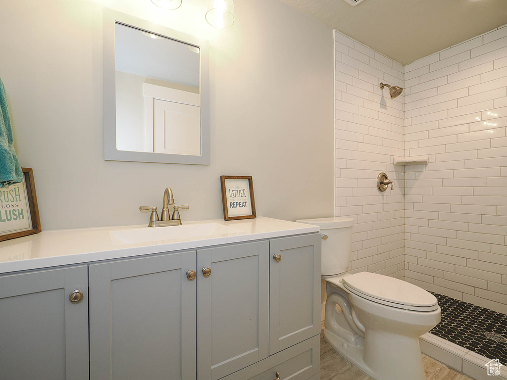 Bathroom with a tile shower, tile flooring, vanity, and toilet