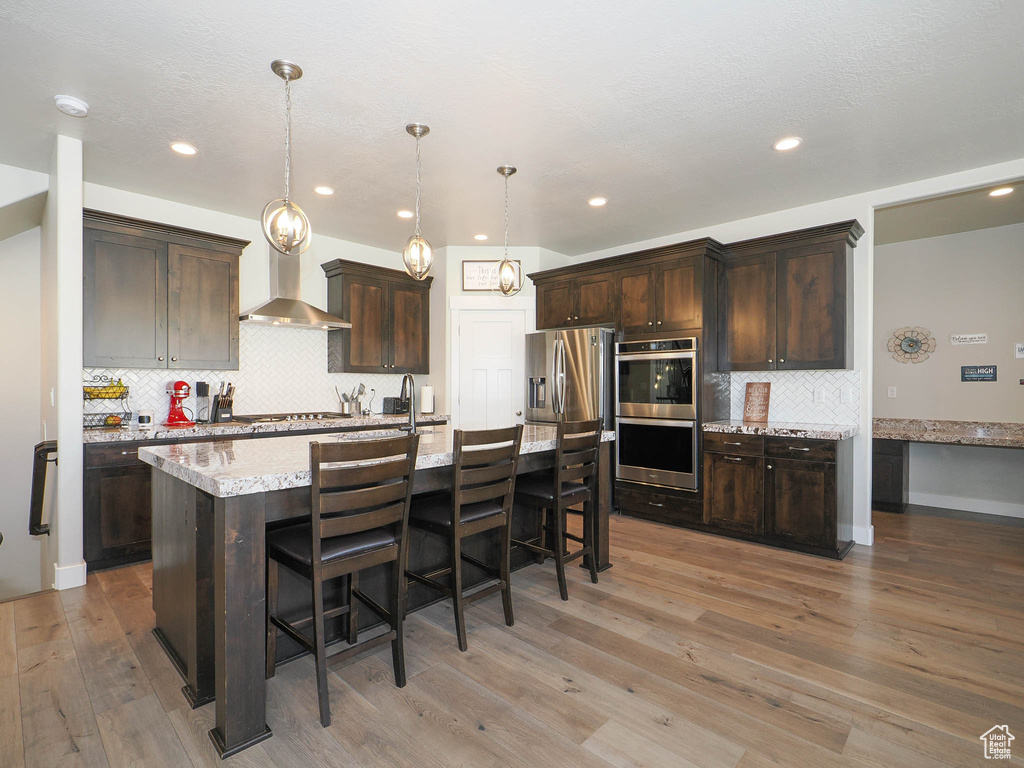 Kitchen with an island with sink, hardwood / wood-style floors, tasteful backsplash, and appliances with stainless steel finishes