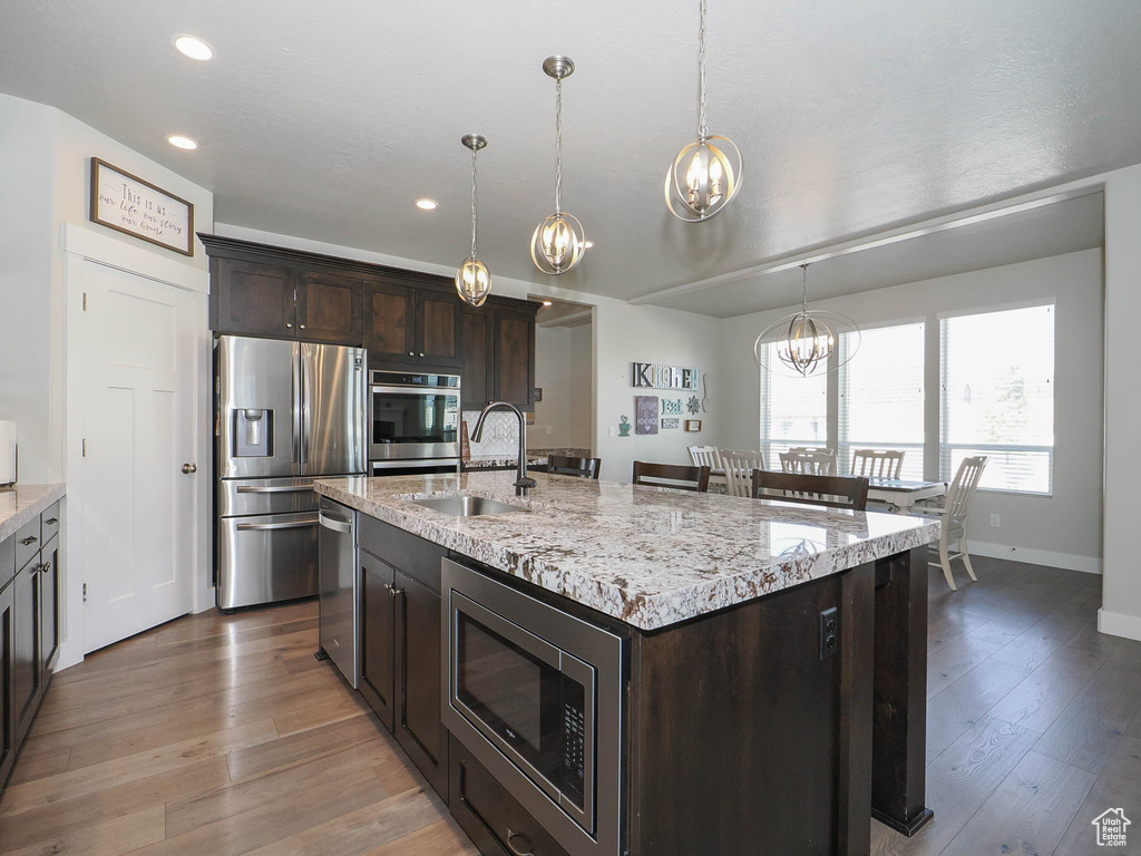 Kitchen featuring hardwood / wood-style floors, stainless steel appliances, decorative light fixtures, sink, and a kitchen island with sink