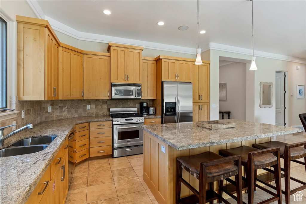 Kitchen featuring tasteful backsplash, stainless steel appliances, decorative light fixtures, a kitchen island, and light tile floors