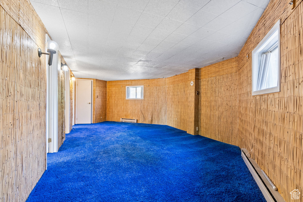 Basement featuring carpet flooring, wood walls, and a baseboard heating unit