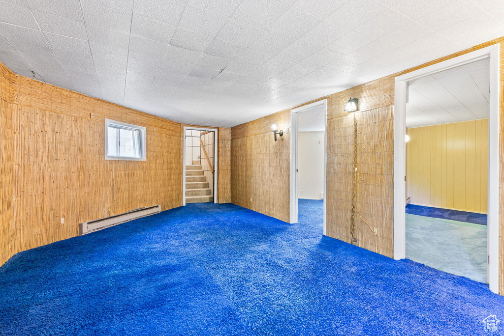 Interior space featuring a baseboard heating unit, wood walls, and dark carpet