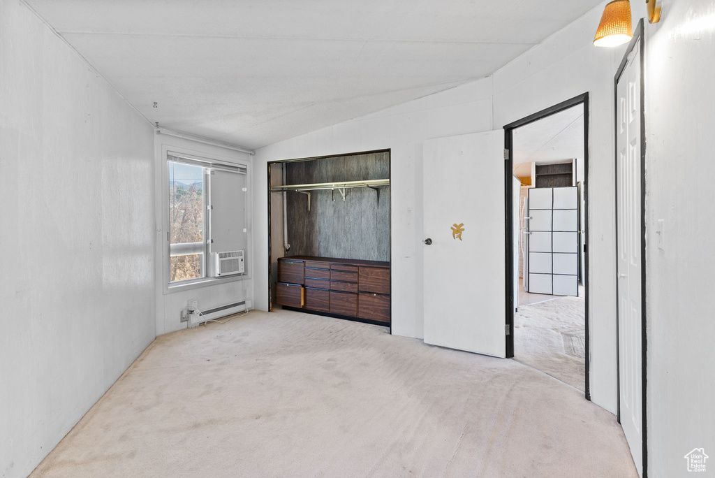 Unfurnished bedroom with a baseboard heating unit, vaulted ceiling, and light colored carpet