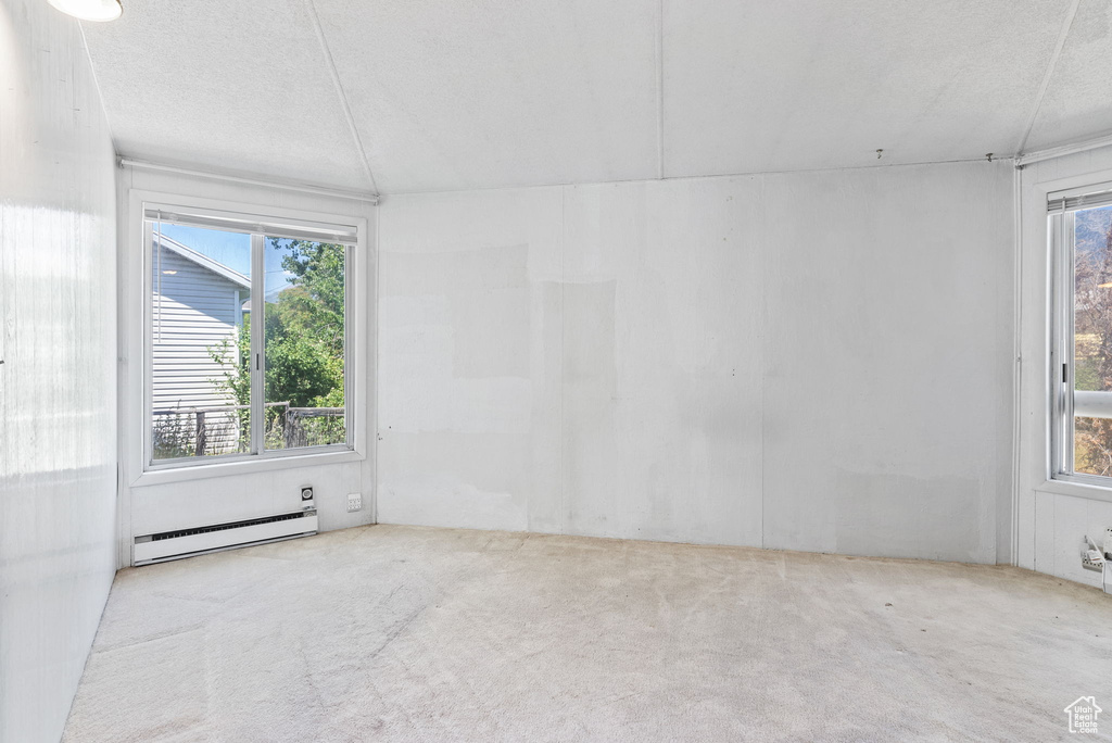 Carpeted empty room featuring a textured ceiling and baseboard heating