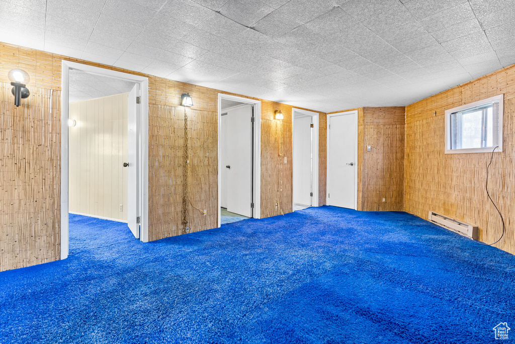 Carpeted empty room featuring wood walls and baseboard heating