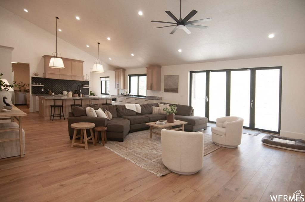 Living room featuring high vaulted ceiling, ceiling fan, and light wood-type flooring