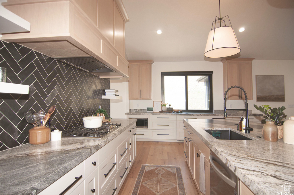 Kitchen featuring light hardwood / wood-style floors, hanging light fixtures, appliances with stainless steel finishes, sink, and tasteful backsplash