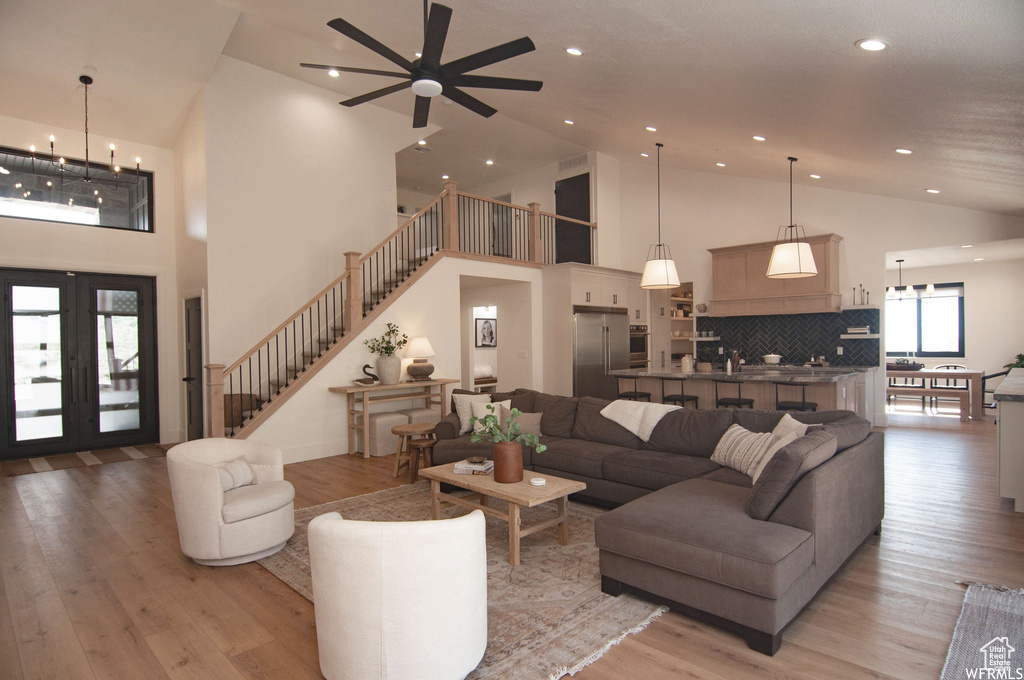 Living room featuring high vaulted ceiling, ceiling fan with notable chandelier, french doors, and hardwood / wood-style flooring