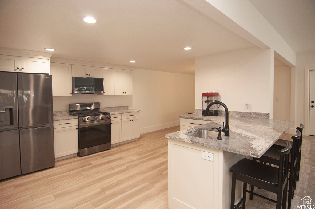 Kitchen with stainless steel appliances, a breakfast bar area, light wood-type flooring, and kitchen peninsula