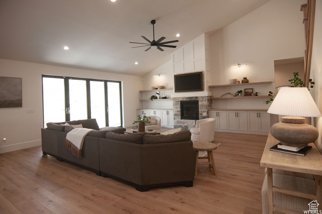 Living room with high vaulted ceiling, ceiling fan, light hardwood / wood-style floors, and a fireplace