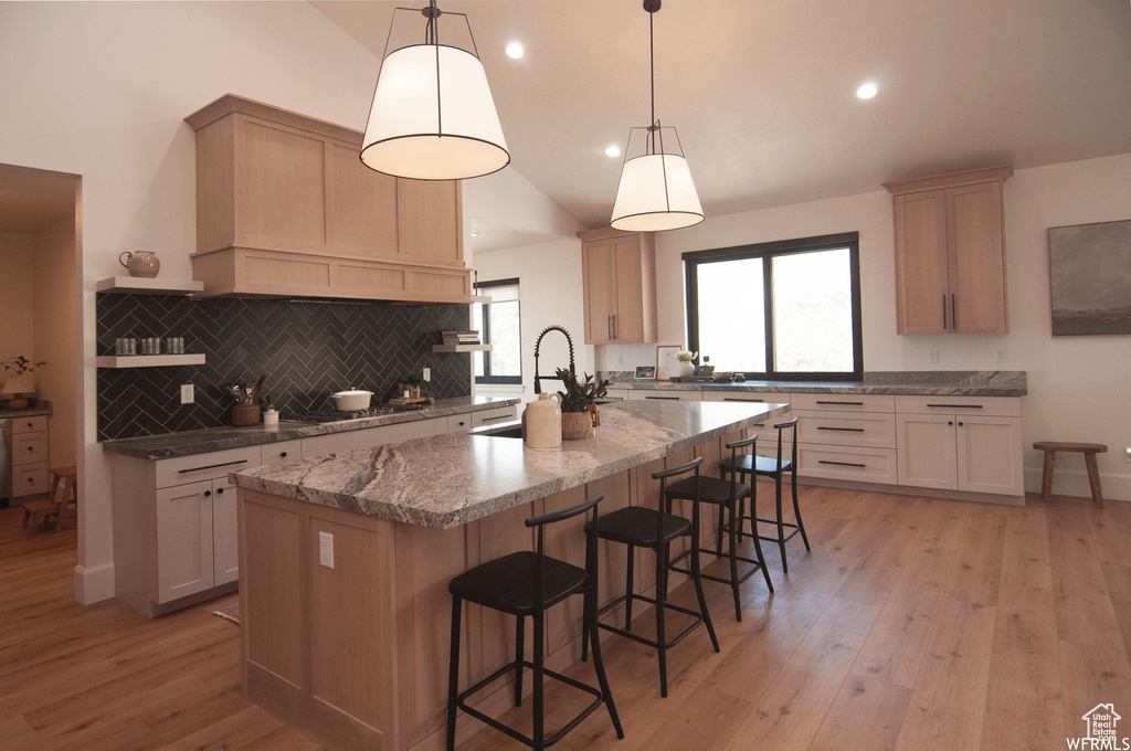 Kitchen featuring light hardwood / wood-style flooring, a kitchen breakfast bar, hanging light fixtures, a center island with sink, and tasteful backsplash